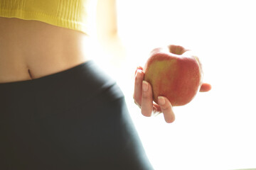 Red apple in a female hand. Young athletic body of a girl in leggings and a top. Fitness and Health