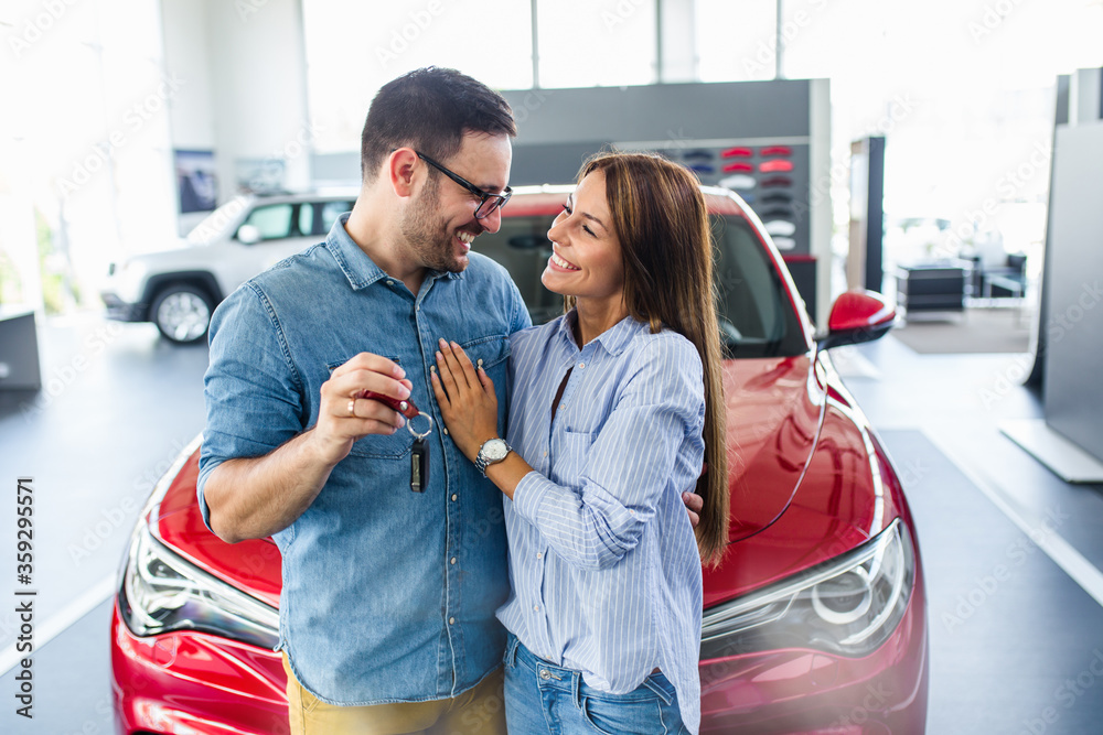 Wall mural beautiful young smiling couple holding a key of their new car.