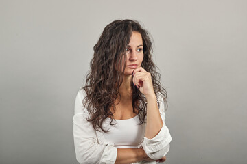 Fototapeta na wymiar Hand on chin thinking about question, pensive expression. Doubt. Thoughtful face. Using that incredibly sharp business mind. Young attractive woman, dressed white blouse, with brown eyes, curly hair