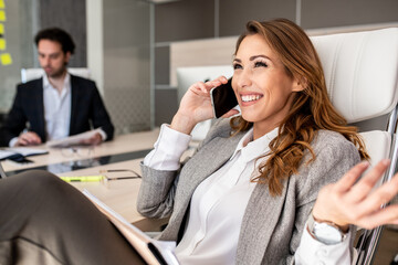 Businesswoman calling with her friend while her colleague is working