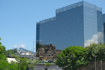 A modern glass tall building which reflects many home in the favelas on the mountain. Wealth and poverty in one frame in Rio de Janeiro.