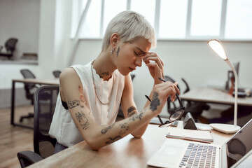 Feeling exhausted. Side view of frustrated young tattooed business woman keeping eyes closed,...