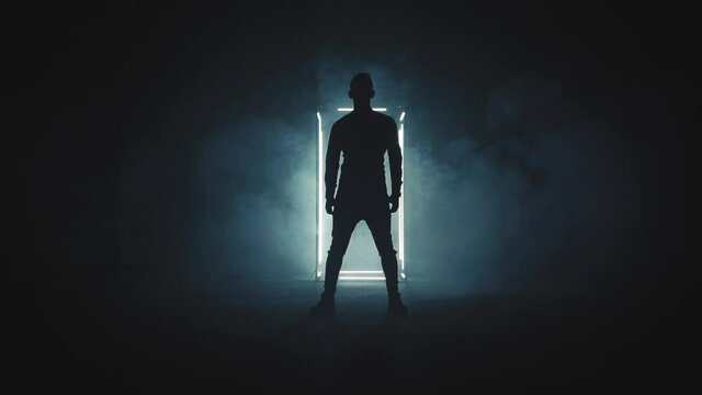 Silhouette of young man standing in the dark smoky room with white light