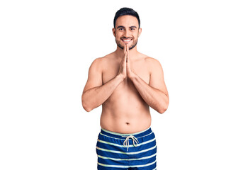 Fototapeta premium Young handsome man wearing swimwear praying with hands together asking for forgiveness smiling confident.