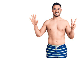 Young handsome man wearing swimwear showing and pointing up with fingers number seven while smiling confident and happy.