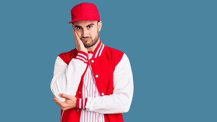 Young handsome man wearing baseball jacket and cap thinking looking tired and bored with depression problems with crossed arms.