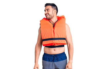 Young handsome man wearing lifejacket looking away to side with smile on face, natural expression. laughing confident.