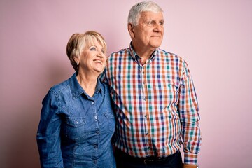 Senior beautiful couple standing together over isolated pink background looking away to side with smile on face, natural expression. Laughing confident.