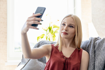 young blonde girl communicates by video call on a smartphone while sitting on a sofa