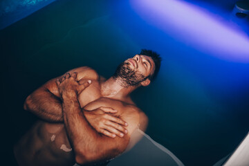 Handsome beard man floating in tank filled with dense salt water used in meditation, therapy, and...