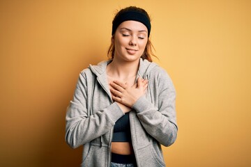 Young beautiful brunette sportswoman wearing sportswear over yellow background smiling with hands on chest with closed eyes and grateful gesture on face. Health concept.