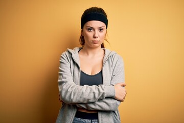 Young beautiful brunette sportswoman wearing sportswear over yellow background skeptic and nervous,...