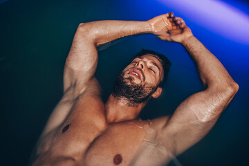Handsome beard man floating in tank filled with dense salt water used in meditation, therapy, and alternative medicine.