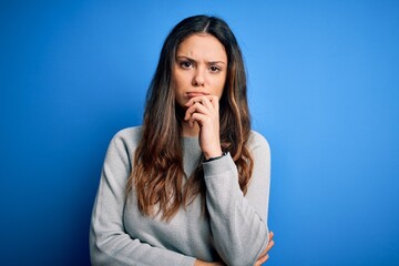 Young beautiful brunette woman wearing casual sweater standing over blue background with hand on chin thinking about question, pensive expression. Smiling with thoughtful face. Doubt concept.