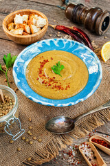 Red lentil cream soup with pepper, spices and parsley in a bowl on napkin and wooden background.