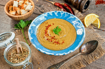 Red lentil cream soup with pepper, spices and parsley in a bowl on napkin and wooden background.