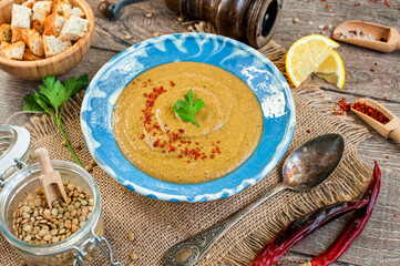 Red lentil cream soup with pepper, spices and parsley in a bowl on napkin and wooden background.