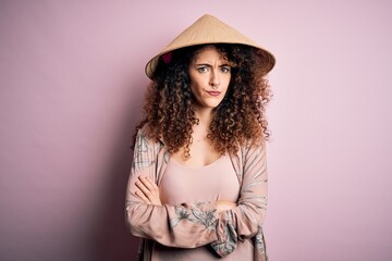 Young beautiful woman with curly hair and piercing wearing traditional asian conical hat skeptic and nervous, disapproving expression on face with crossed arms. Negative person.