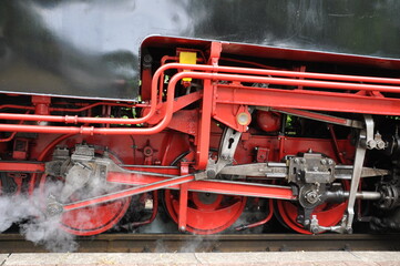 rote Antriebsräder mit Pleuelstangen einer alten Dampflok und austretendem Dampf
