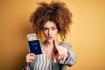 Young beautiful woman with curly hair and piercing holding Germany passport id and dollars pointing with finger to the camera and to you, hand sign, positive and confident gesture from the front