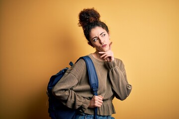 Young beautiful student woman with curly hair and piercing wearing backpack serious face thinking about question, very confused idea