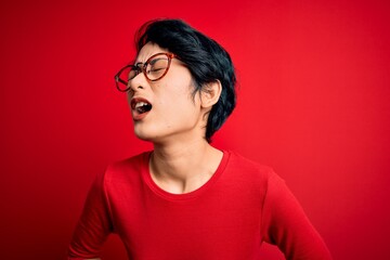 Young beautiful asian girl wearing casual t-shirt and glasses over isolated red background with hand on stomach because nausea, painful disease feeling unwell. Ache concept.