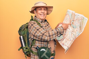 Fototapeta premium Senior man with grey hair wearing hiker backpack holding map smiling happy pointing with hand and finger