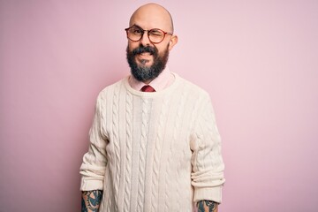 Handsome bald man with beard and tattoo wearing glasses and sweater over pink background winking looking at the camera with sexy expression, cheerful and happy face.