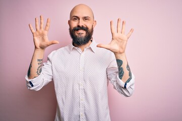 Naklejka premium Handsome bald man with beard wearing elegant shirt over isolated pink background showing and pointing up with fingers number ten while smiling confident and happy.