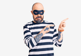 Naklejka premium Young handsome man wearing burglar mask pointing aside worried and nervous with both hands, concerned and surprised expression