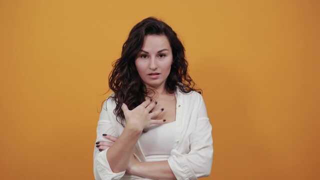 Standing and cross her arms on chest. Young attractive woman, dressed white blouse, with brown eyes, curly hair, yellow background