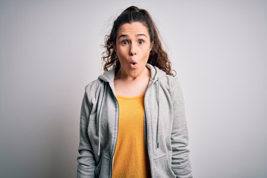 Young beautiful sportswoman with curly hair wearing sportswear over white background afraid and shocked with surprise expression, fear and excited face.