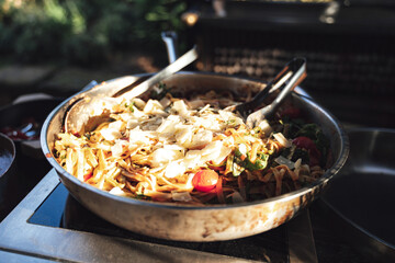 Closeup of pan with pasta salad with vegetable and parmesan cheese. Outdoor kitchen. Celebration, party, birthday or wedding concept.