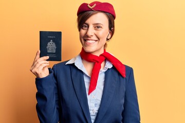 Young beautiful woman wearing stewardess uniform holding canadian passport looking positive and happy standing and smiling with a confident smile showing teeth
