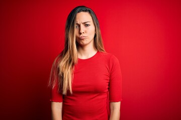 Young beautiful blonde woman with blue eyes wearing casual t-shirt over red background depressed and worry for distress, crying angry and afraid. Sad expression.
