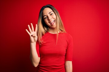 Young beautiful blonde woman with blue eyes wearing casual t-shirt over red background showing and pointing up with fingers number four while smiling confident and happy.