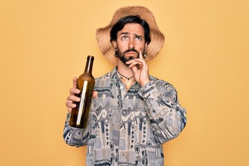 Young handsome hispanic bohemian hipster man with bear drinking from a empty wine bottle serious...