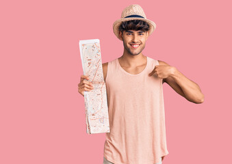 Young hispanic man wearing summer hat holding map pointing finger to one self smiling happy and...