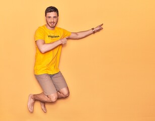 Fototapeta na wymiar Young handsome hispanic man wearing t shirt with happiness word message smiling happy. Jumping with smile on face over isolated yellow background