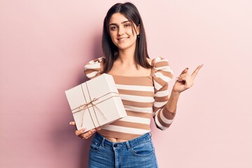 Young beautiful girl holding gift smiling happy pointing with hand and finger to the side