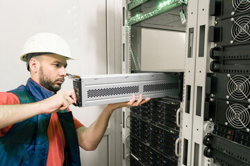 An engineer installs a new battery pack into an uninterruptible power supply. Replacing the power module in the server room rack. Maintenance of data center equipment. - obrazy, fototapety, plakaty