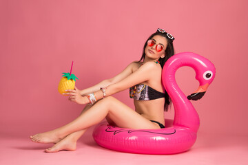 Obraz na płótnie Canvas beautiful young woman in bikini with big pink flamingo toy , isolated on pink background. blond girl smiling, posing with beach accessorize . beach summer concept, tropical vibe, studio shot