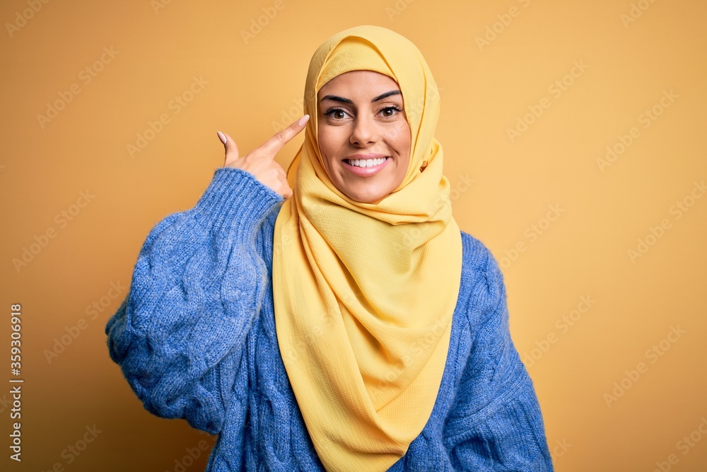 Sticker young beautiful brunette muslim woman wearing arab hijab over isolated yellow background smiling poi