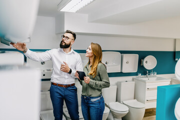 Fototapeta premium Middle age man choosing ceramic tiles and utensils for his home bathroom and female seller helps him to make right decision