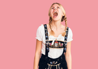 Young beautiful blonde woman wearing oktoberfest dress angry and mad screaming frustrated and...