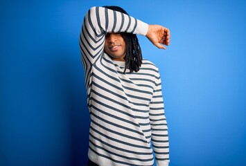 Young handsome african american afro man with dreadlocks wearing casual striped sweater covering eyes with arm, looking serious and sad. Sightless, hiding and rejection concept