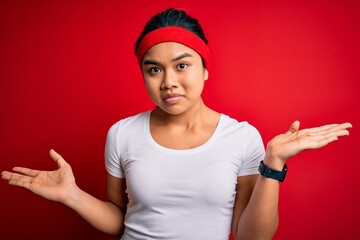 Young beautiful asian sporty woman wearing sportswear doing sport over red background clueless and...