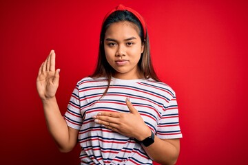 Young beautiful asian girl wearing casual striped t-shirt over isolated red background Swearing...