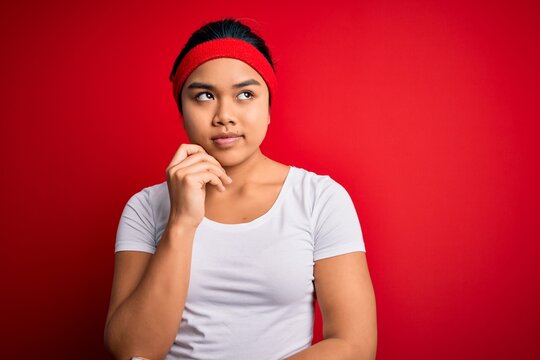 Young beautiful asian sporty woman wearing sportswear doing sport over red background with hand on chin thinking about question, pensive expression. Smiling with thoughtful face. Doubt concept.