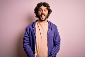 Obraz premium Young handsome sporty man with beard wearing casual sweatshirt over pink background sticking tongue out happy with funny expression. Emotion concept.